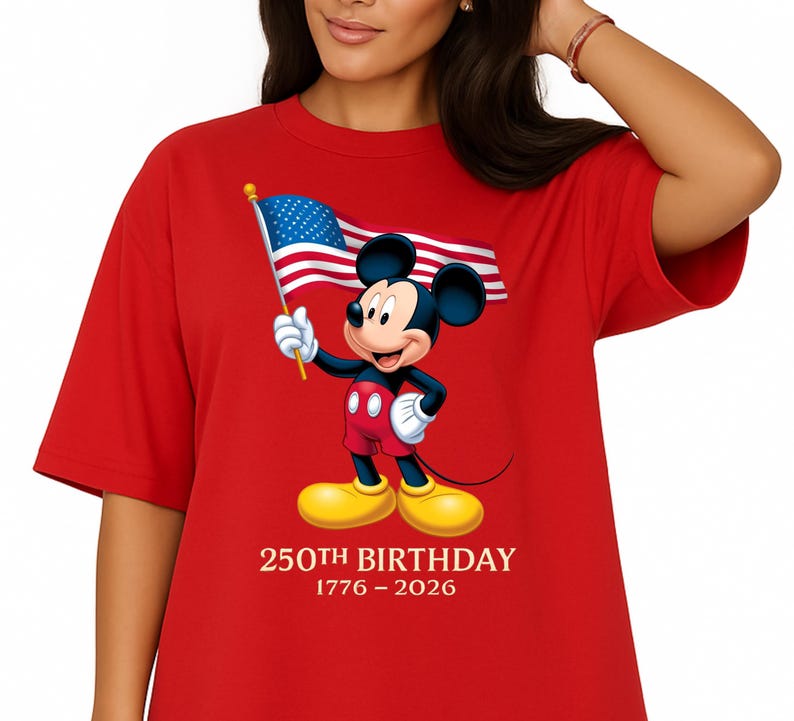 Puede incluir: Camiseta roja con Mickey Mouse sosteniendo una bandera estadounidense. Mickey lleva pantalones cortos rojos, guantes blancos y zapatos amarillos. El texto "250TH BIRTHDAY 1776-2026" est&aacute; impreso debajo.