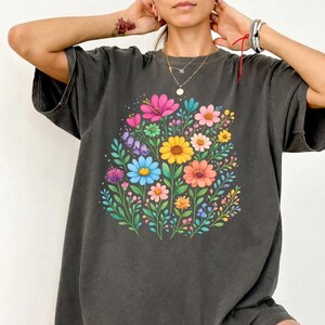 May include: Dark gray t-shirt featuring a vibrant floral design. The graphic showcases a bouquet of colorful flowers, including pink, yellow, blue, and orange blooms, surrounded by green leaves. The shirt has short sleeves and a relaxed fit.