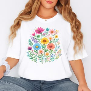 May include: White t-shirt featuring a vibrant floral design. The design includes a variety of colorful flowers in shades of pink, yellow, blue, and orange, surrounded by green leaves. The shirt is a casual, comfortable style.