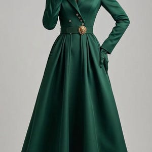 Könnte beinhalten: Ein bodenlanges, smaragdgrünes Mantelkleid mit langen Ärmeln, Reverskragen und doppelreihiger Knopfleiste. Das Kleidungsstück verfügt über einen passenden Gürtel mit einer goldenen Löwenkopf-Schnalle sowie dazu passende grüne Handschuhe.