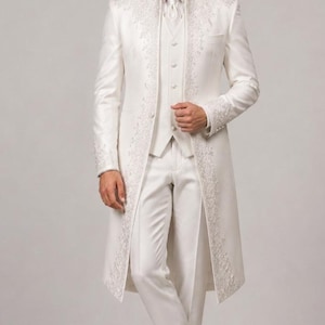 May include: A formal white suit with intricate floral embroidery. The ensemble includes a long coat, vest, and trousers. The suit is paired with white dress shoes, creating a sophisticated and elegant look.