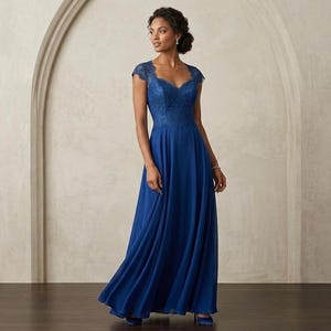 May include: A long, flowing, royal blue gown with a lace bodice and cap sleeves. The dress has a V-neckline and a full skirt. The woman is wearing a bracelet and matching blue heels. The background is a neutral colour.