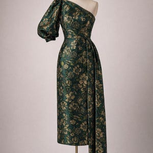 May include: Aurelia one-shoulder gown in dark green fabric with gold floral pattern. The dress features a single puffed sleeve and a flowing skirt with a train. Couture Sewing Pattern Sizes 00-32.