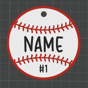 Puede incluir: Adorno con tem&aacute;tica de b&eacute;isbol con fondo blanco, costuras rojas y borde rojo. La palabra "NAME" est&aacute; impresa en letras negras en negrita, con el n&uacute;mero "1" debajo. Hay un agujero en la parte superior para colgar.