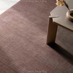 May include: A solid, deep brown area rug with a short, dense pile texture. The rug features a uniform, muted earth-tone color throughout its surface. The text Classy Decor Rug is visible in two locations on the rug surface in a light gray font.