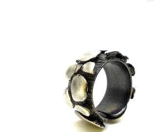 May include: A silver ring with a textured band and a design of overlapping circles. The ring is made of metal and has a dark gray finish.
