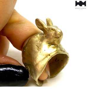 Peut inclure: Une bague en forme de lapin en or, avec la tête du lapin formant le haut de la bague. La bague est portée sur un doigt.