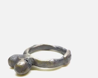 May include: A handcrafted, silver-toned ring with a unique, organic design. The ring features a textured band and a cluster of three rounded shapes, creating a sculptural and artistic aesthetic. The ring is set against a white background.