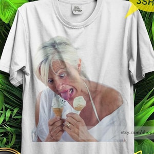 Könnte beinhalten: Ein weißes kurzärmeliges T-Shirt mit einem Fotodruck einer Person mit blonden Haaren, die ein weißes Oberteil trägt, zwei Eiswaffeln hält und die Zunge herausstreckt. Das T-Shirt hat einen Rundhalsausschnitt und eine Standardpassform.