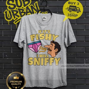 May include: A heather gray short-sleeve t-shirt featuring a graphic print of a pair of pink underwear and a cartoon face with a mustache. The text reads IF IT'S FISHY I WILL SNIFFY in yellow letters. The shirt has a crew neckline and a standard fit.
