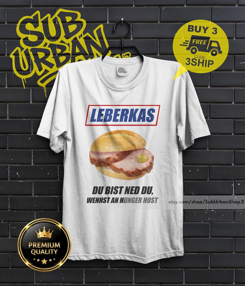 May include: White t-shirt featuring a graphic of a Leberkas sandwich with the word "LEBERKAS" above it. The shirt also has text that reads "DU BIST NED DU, WENNST AN HUNGER HOST". A yellow circle says "BUY 3 FREE" and "3SHIP".