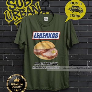 May include: Olive green t-shirt featuring a graphic of a Leberkas sandwich with mustard. The word "LEBERKAS" is above the sandwich in a white and red box. Below the sandwich is the text "DU BIST NED DU, WENNST AN HUNGER HOST".