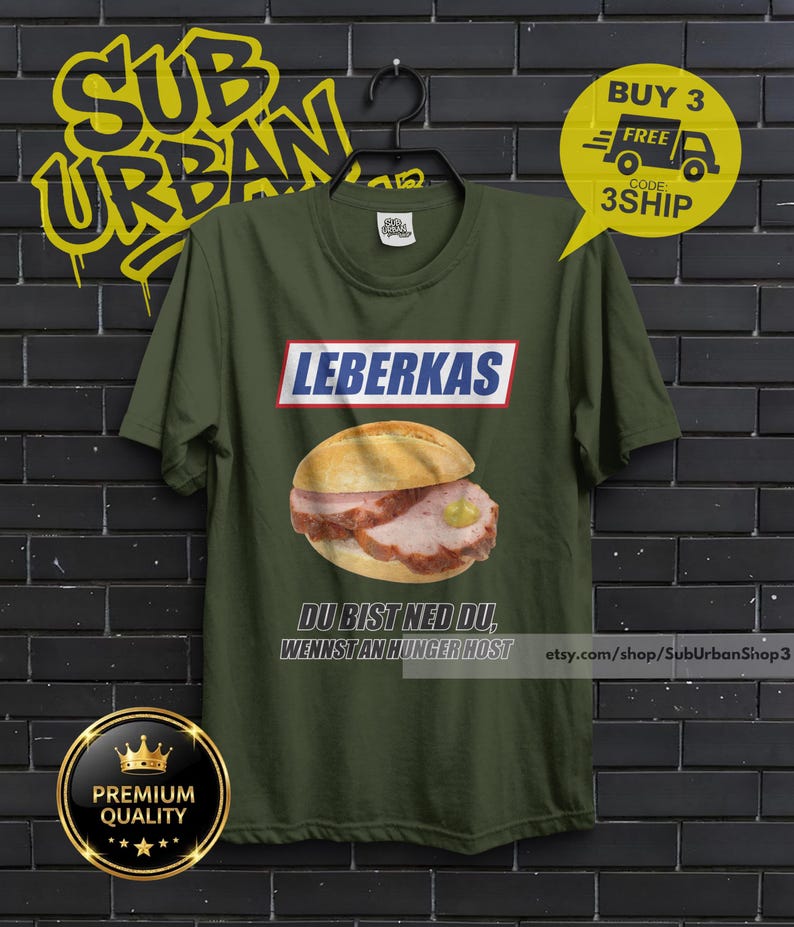 May include: Olive green t-shirt featuring a graphic of a Leberkas sandwich with mustard. The word "LEBERKAS" is above the sandwich in a white and red box. Below the sandwich is the text "DU BIST NED DU, WENNST AN HUNGER HOST".