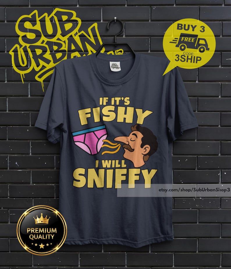 May include: A dark gray short-sleeve t-shirt featuring a graphic of a person with a mustache sniffing a pair of pink underwear. The text on the shirt reads IF IT'S FISHY I WILL SNIFFY in bold yellow letters. The shirt is displayed on a black hanger.