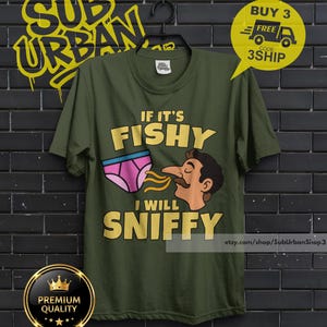 May include: An olive green t-shirt featuring a graphic of a person sniffing a pair of pink underwear. The text reads IF IT'S FISHY I WILL SNIFFY in bold yellow letters. The shirt has a crew neck and short sleeves, displayed on a black hanger.