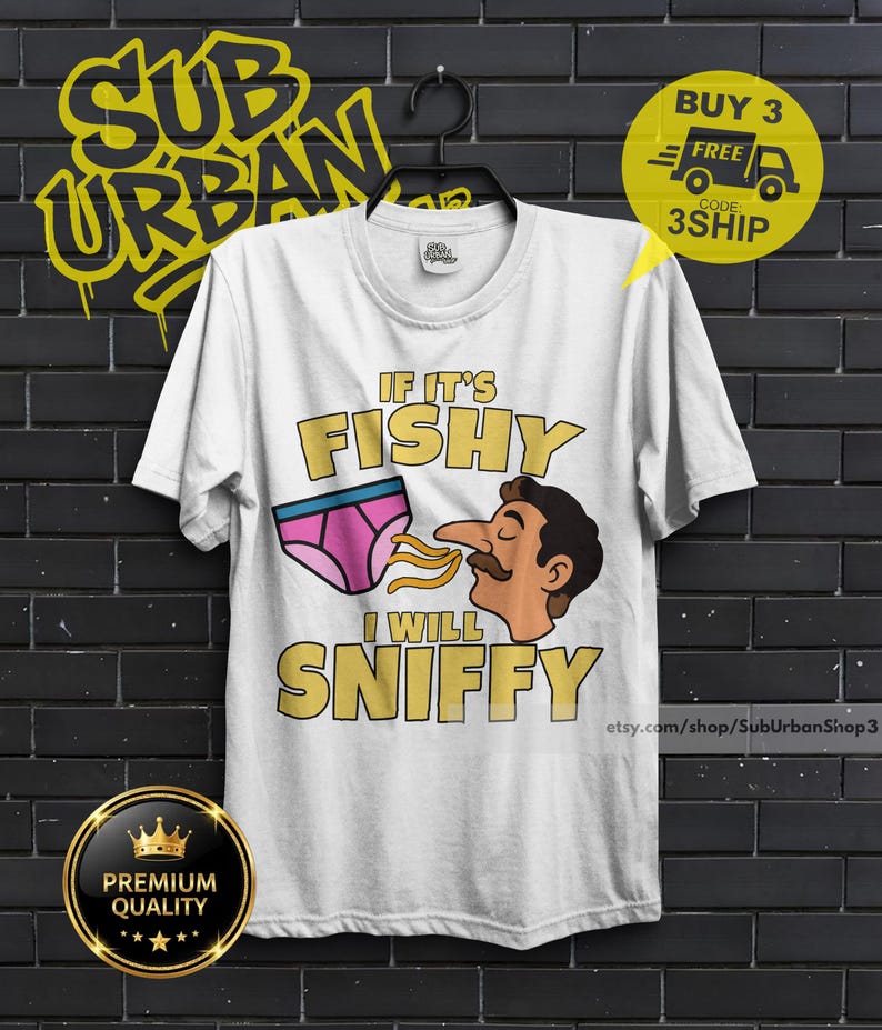 May include: A white short-sleeve t-shirt featuring a graphic of pink underwear and a cartoon face with a mustache. The text reads IF IT'S FISHY I WILL SNIFFY in yellow block letters. The shirt has a crew neckline and is displayed on a black hanger.
