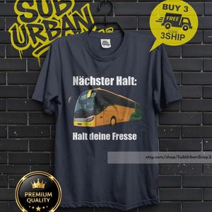 May include: Dark navy blue t-shirt with a graphic of a yellow and green bus and the text "N&auml;chster Halt: Halt deine Fresse". The shirt also features the text "SUB URBAN" in yellow graffiti style.