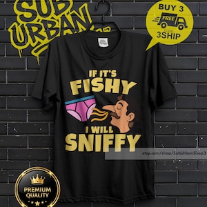 May include: A black short-sleeved t-shirt featuring a graphic print of pink underwear and a person sniffing them. The text reads IF IT'S FISHY I WILL SNIFFY in yellow capital letters. The shirt has a crew neckline and is displayed on a black hanger.