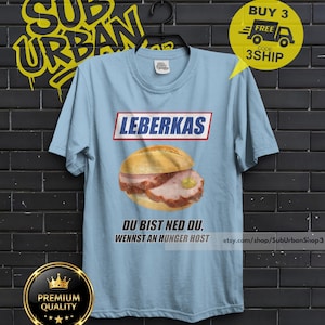 May include: Light blue t-shirt featuring a Leberkas sandwich graphic with the text "LEBERKAS" above and "DU BIST NED DU, WENNST AN HUNGER HOST" below. The shirt also has a "BUY 3 FREE" promotion graphic.
