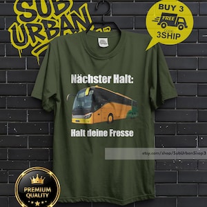 May include: Olive green t-shirt with a bus graphic and German text. The text reads "N&auml;chster Halt: Halt deine Fresse." A yellow sticker says "Buy 3 Free" with a code. The shirt hangs on a black hanger.