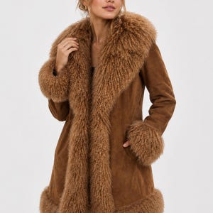 May include: A brown suede coat featuring a wide, textured curly fur collar, matching fur cuffs at the sleeves, and a fur-trimmed hemline. The coat has a smooth suede body with long sleeves and a straight silhouette that reaches mid-thigh length.