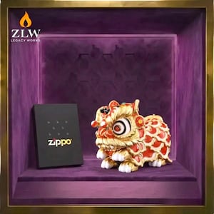 May include: A display case featuring a gold-colored lion statue with red accents and a black Zippo box. The lion has detailed features and sits on a purple velvet surface. The case has a gold frame and the Zippo box has the brand name in white.