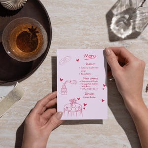 Könnte beinhalten: Eine hellviolette, rechteckige Menükarte mit dunkelrosa handgezeichneten Illustrationen von Eheringen, einem Champagner-Turm und einem gedeckten Tisch mit Herzen. Der Text listet Vorspeisen, Hauptgerichte und Desserts auf, darunter Pilzsuppe, Lachs und Crème Brûlée.