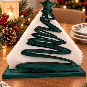 May include: A dark green, 3D-printed napkin holder shaped like a stylised Christmas tree with a star topper. The holder features a textured, layered design and holds a stack of white, triangular-folded paper napkins in an upright position.