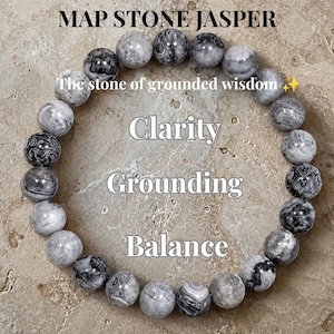 Peut inclure: Un bracelet circulaire composé de perles rondes et lisses en jaspe peau de serpent dans des tons de gris, noir et blanc. Le texte MAP STONE JASPER, The stone of grounded wisdom, Clarity, Grounding, and Balance est superposé sur les perles.
