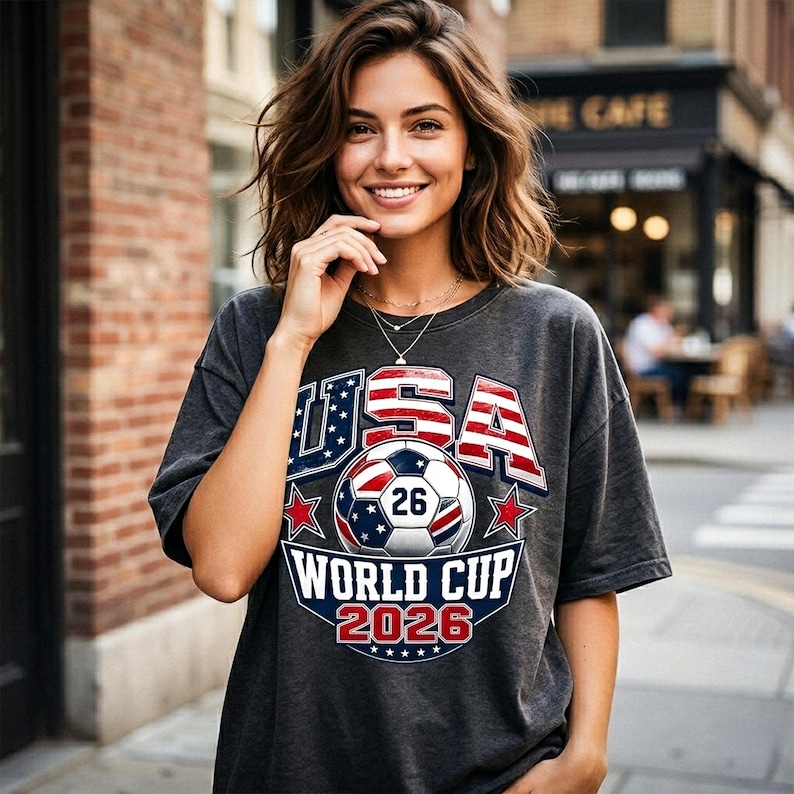 Pu&ograve; includere: T-shirt grigio scuro con grafica USA World Cup 2026. Il design presenta un pallone da calcio, stelle e la scritta "USA" in rosso e blu. La maglietta &egrave; in stile casual.