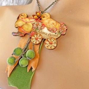 May include: A wooden pendant necklace with a vintage Easter image of two chicks pulling a wagon with the text "A Joyful Easter". The pendant is attached to a green velvet ribbon with brown and green felt balls.