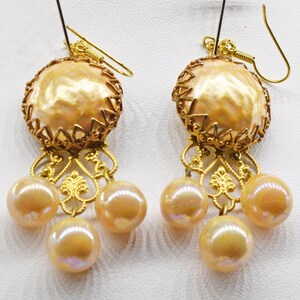 May include: A pair of gold earrings with a large, round, pearl-like drop and a smaller pearl-like drop hanging from the bottom. The earrings have a delicate, filigree design.