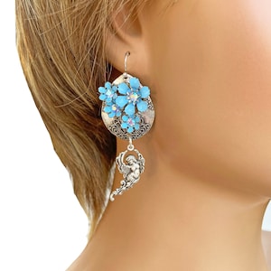 May include: Silver dangle earrings with a blue flower cluster and a silver angel charm.
