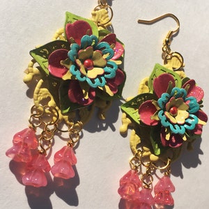 Puede incluir: Un par de pendientes florales con flores rosas, amarillas, verdes y azules. Los pendientes tienen ganchos dorados y cuelgan cuentas de cristal rosa.