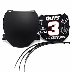May include: A black motorcycle front number plate with mounting tabs, a matching black plate featuring the text GUTS, GS CUSTOMS, the number 3 in white with a red outline, and various white graphic logos including Red Bull and a fox head icon.