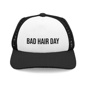 Peut inclure: Casquette de camionneur noire et blanche avec le texte "BAD HAIR DAY" en lettres noires grasses. La casquette a un panneau avant blanc, une visière noire et un dos en filet noir. La casquette a une visière incurvée et une fermeture à pression.