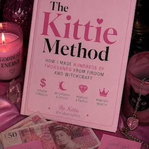 May include: A light pink hardcover book titled The Kittie Method, featuring the subtitle How I Made Hundreds of Thousands from Findom and Witchcraft, with icons for strategy, spells, mindset, and wealth, authored by Kittie @sugarnatrix.