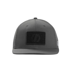 May include: A charcoal gray baseball cap with a curved brim and a structured crown. The cap features a black rectangular patch on the front with a geometric logo. The sides of the cap have small perforations for ventilation. A stylish accessory for outdoor activities.