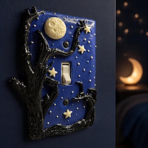 Op de afbeelding: Een rechthoekige lichtschakelaarplaat met een donkerblauwe nachthemelachtergrond, een verhoogd, getextureerd zwart boomsilhouet, een crèmekleurige maan en verschillende kleine crèmekleurige sterren verspreid over het oppervlak met twee zwarte schroeven.