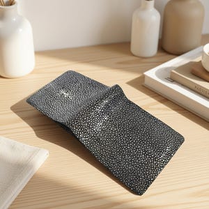 Peut inclure: Un portefeuille pliable présentant une surface texturée noire et argentée avec un motif de petites bosses arrondies semblables à des perles. Le portefeuille est légèrement ouvert, révélant une doublure intérieure sombre et un motif tacheté.