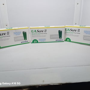 Op de afbeelding: Drie dozen UA Sure II bloedurinezuurteststrips worden getoond. Elke doos is wit met groene en zwarte tekst en afbeeldingen. De dozen hebben het nummer 25 erop. De merknaam ApexBio is ook zichtbaar.