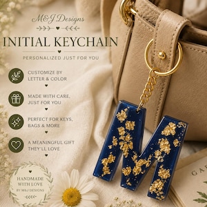 Op de afbeelding: Een donkerblauwe hars sleutelhanger in de vorm van de letter M met ingebedde bladgoudvlokken, bevestigd aan een goudkleurige metalen ketting en ring. De tekst M&J Designs INITIAL KEYCHAIN PERSONALIZED JUST FOR YOU is zichtbaar met iconen.