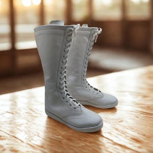 May include: A pair of tall, white lace-up boots featuring a smooth finish, a rounded toe, and a flat sole. The boots extend to the mid-calf and are secured with white laces that run up the front center, providing a clean and uniform appearance.