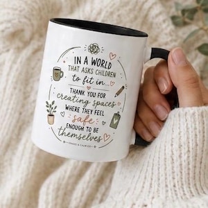 May include: A white ceramic mug with a black rim and handle, featuring the printed text: IN A WORLD THAT ASKS CHILDREN to fit in... THANK YOU FOR CREATING SPACES WHERE THEY FEEL safe ENOUGH TO BE themselves. Includes small illustrations of a mug, plant, pencil, and clipboard.