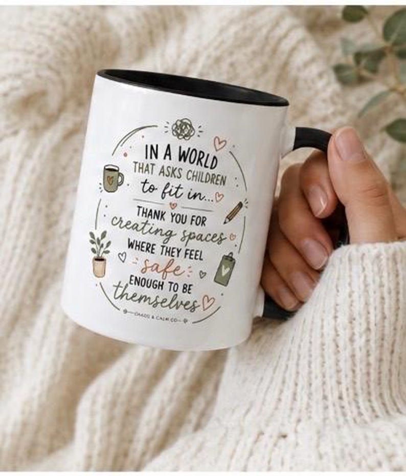 May include: A white ceramic mug with a black rim and handle, featuring the printed text: IN A WORLD THAT ASKS CHILDREN to fit in... THANK YOU FOR CREATING SPACES WHERE THEY FEEL safe ENOUGH TO BE themselves. Includes small illustrations of a mug, plant, pencil, and clipboard.