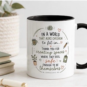 May include: A white ceramic mug with a black handle and interior rim. The mug features the text: IN A WORLD THAT ASKS CHILDREN TO FIT IN... THANK YOU FOR CREATING SPACES WHERE THEY FEEL SAFE ENOUGH TO BE THEMSELVES, surrounded by small illustrations.