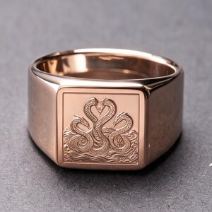 Könnte beinhalten: Ein Siegelring aus Roségold mit einer quadratischen Platte, die eine detaillierte Gravur von drei ineinander verschlungenen Schlangen zeigt, die aus stilisierten Wellen aufsteigen. Das Metall hat eine polierte Oberfläche und eine breite Ringschiene.