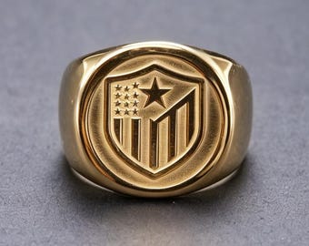 Anillo con escudo heráldico americano de oro de 18 quilates, redondo y con borde puntiagudo, de banda sólida.