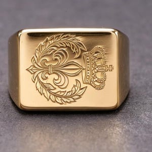 May include: A gold-colored signet ring with a rectangular face. The face features an engraved design of a fleur-de-lis, a crown, and a cross. The ring has a polished finish.