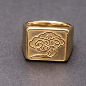 Könnte beinhalten: Ein goldfarbener Siegelring mit quadratischer Platte, die ein eingraviertes, stilisiertes Wolkenmuster zeigt. Das Metall hat eine polierte Oberfläche am Ringband und eine matte Textur auf der quadratischen Platte mit der Wolkengravur.